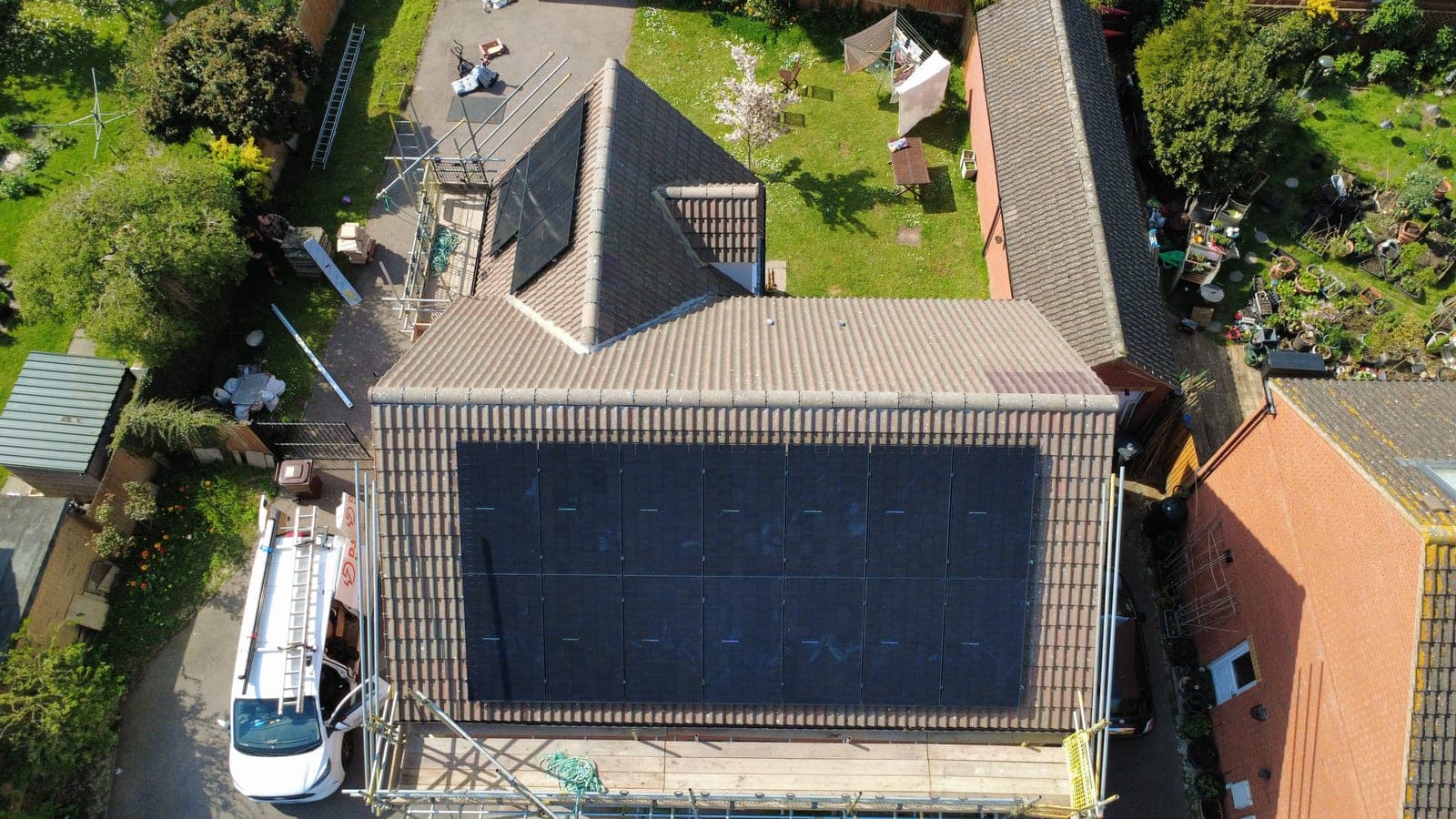 Drone aerial of a Djuka rooftop solar install on a Midlands home with the branded van and scaffolding visible