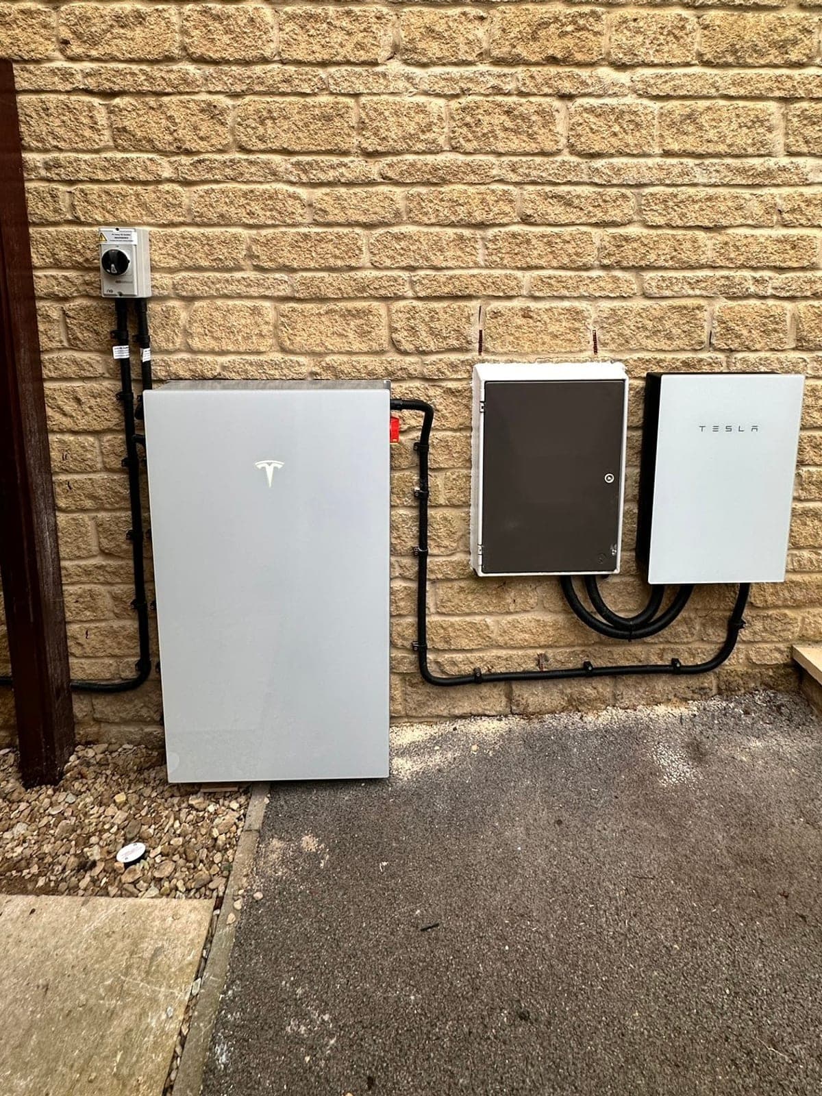 Tesla Powerwall and Tesla backup gateway installed clean on a cream brick wall